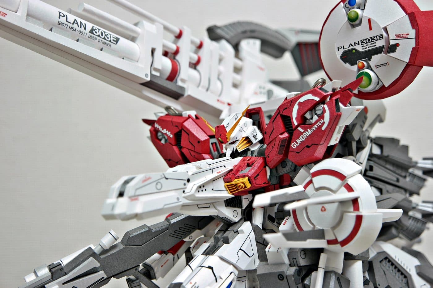 PLAN 303E 표기가 찍힌 캐논과 GUNDAM SYSTEM 글자가 새겨진 붉은 흉부, 금색 안테나가 드러난 상반신 클로즈업