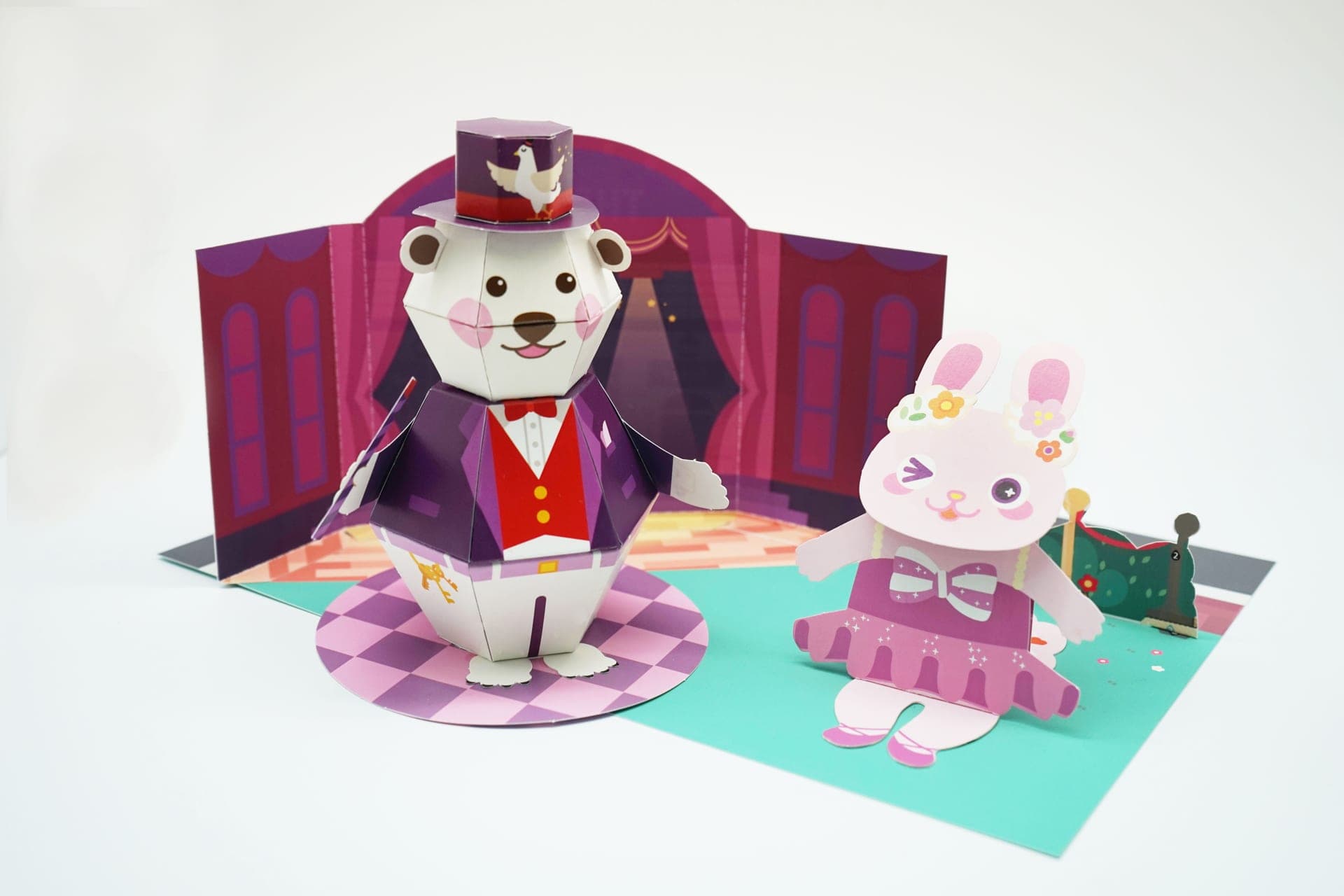 오리 그림 모자를 쓰고 지팡이를 든 곰 마술사와 분홍 튜튜 차림 토끼 발레리나가 붉은 무대 배경 앞에 선 페이퍼토이